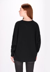 Černá oversized mikina s kleslými rameny, kulatým výstřihem a žebrovanými manžetami. Tkanina vypadá měkce a má jemně strukturovaný povrch.