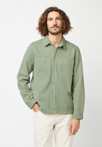 Green button-up shirt with two chest pockets, made of soft cotton material, featuring a collar and long sleeves. Light texture visible.