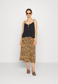 Top preto sem mangas com um detalhe de nó, combinado com uma saia midi fluida de padrão leopardo em laranja e preto, usada com sandálias pretas com tiras.