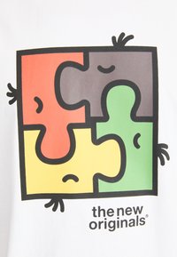 Weißes T-Shirt mit einem bunten Puzzlemuster in Rot, Grün, Gelb und Grau, das cartoonartige Gesichter zeigt. Logo "the new originals" darunter.