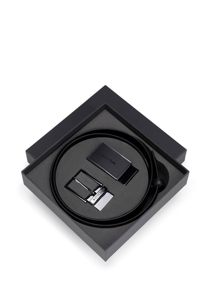 Ceinture en cuir noir présentée dans une boîte carrée noire, avec une boucle noire texturée et un accent en métal argenté. Comprend une pièce de boucle supplémentaire.