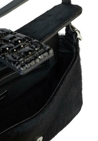 Borsa nera con esterno morbido simile a pelliccia. Presenta una chiusura gioiello e un scomparto con cerniera interno, che mostra una fodera liscia di tessuto scuro.