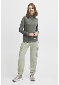 Sudadera gris con cordón, pantalones cargo verde claro a juego y zapatillas deportivas en tonos neutros con patrones texturizados y acentos.