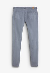 Jeans ajustados de color gris claro, confeccionados en denim con una textura suave; presentan cinco bolsillos y un parche de cuero en la cinturilla.