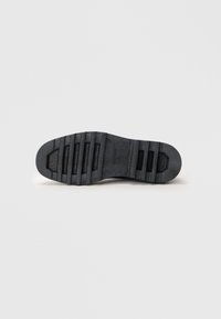 Semelle de chaussure en caoutchouc noir avec une surface texturée, comportant des rainures horizontales et une pointe arrondie. Motif de semelle clairement défini pour une meilleure adhérence.