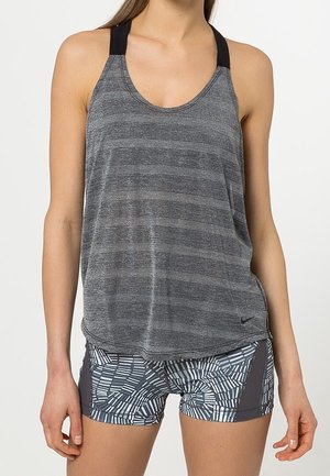 Vrouw draagt een mouwloze grijze gestreepte tanktop en grijze sportshorts met patroon, staat met ontspannen armen langs het lichaam.