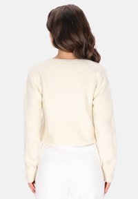 Suéter de color crema, de punto, con mangas largas y escote redondo. Tejido texturizado y corte corto, visto desde la parte posterior.