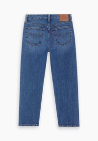 Jean en denim bleu vu de dos avec deux poches cousues, un patch en cuir marron de marque et une étiquette en tissu rouge sur la poche droite.
