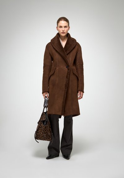 Brūna šerlinga mētelis ar plašu apkakli, divām priekšējām kabatām un vienu pogu aizdari. Apvienots ar pelēkiem platām biksēm un leopardu raksta somu.