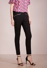 Pantaloni neri slim-fit con dettagli in zip argentati, abbinati a una maglietta con motivo floreale. Tessuto morbido, design su misura, lunghezza alla caviglia.