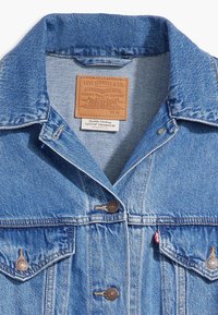 Ljusblå denimjacka med två framfickor, knapplås och en läderetikett sydd i kragen. Stickad detaljer och kopparknappar.