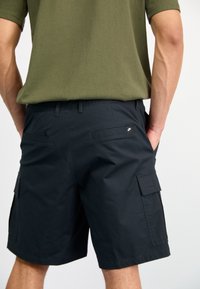 Black cargo shorts with multiple side pockets, made of lightweight fabric. Features a elastic waist and a small Nike logo near the back pocket.