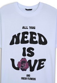 Maglietta bianca in cotone con testo grande nero che recita "TUTTO QUELLO DI CUI HAI BISOGNO È AMORE" e un'immagine di rosa maroon, accompagnata dalla scritta "E FIORI FRESCHI."