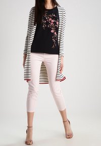 Top nero con ricami floreali, cardigan lungo a righe, pantaloni cropped rosa chiaro e sandali con tacco. Il cardigan ha dettagli rossi.
