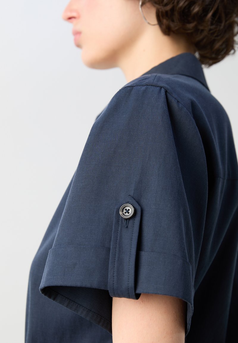 Marineblaues Kurzarmhemd mit strukturiertem Design, gerollten Ärmeln, einem Knopfdetail am Ärmel und einer glatten Textur.