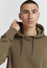 Pruun kapuutsiga sweatshirta, mis on valmistatud pehmest kangast, sisaldab nööriga kapuutsit, soonikkoes mansette ning on vabalt suudeldav. Sile tekstuur ja minimaalne detailsus.