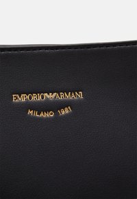 Czarna skóra z tłoczonym złotym napisem "EMPORIO ARMANI MILANO 1981", charakteryzująca się gładką teksturą i czystymi krawędziami.