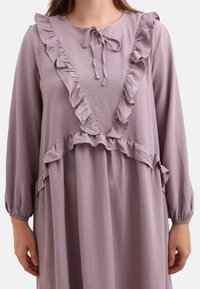 Vestito lavanda con maniche lunghe, caratterizzato da accenti arricciati lungo il colletto e l'orlo, e una vestibilità ampia. La trama appare leggera e fluida.