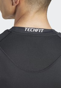 Zwart aansluitend sportshirt met een gladde textuur, voorzien van een ronde halslijn en het "TECHFIT"-logo in het wit op de achterkant nabij de kraag.