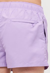 Shorts de baie mov, confecționați dintr-un material ușor, cu un brâu elastic, buzunare laterale și un buzunar pe spate cu închidere cu fermoar.