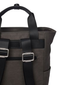 Sac à dos en tissu gris avec des bretelles noires, une poignée supérieure, des éléments en argent et une poche zippée à l'avant. Il a une forme structurée et une poche latérale.