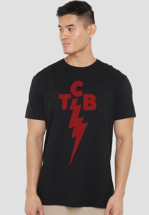 Young man wearing black T-shirt with red letters "C T B" and a lightning bolt design, looking to his left against a plain background.