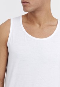 Weißes Tanktop mit breiten Schulterträgern, aus weichem, leichtem Material. Verfügt über einen runden Halsausschnitt und ein minimalistisches Design.