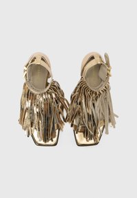 Gold sandals with fringe detail, featuring a square toe, a metallic sheen, and a strap at the ankle. Smooth texture and minimalistic design.