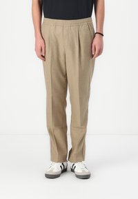 Pantalones plisados beige con cinturilla el�ástica, de corte recto y con dos bolsillos laterales, combinados con zapatillas blancas y negras.