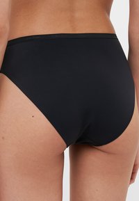 Black high-waisted briefs made of smooth fabric with a seamless design and an elastic waistband featuring the Calvin Klein logo.