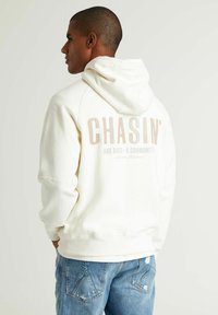 Witte hoodie met een groot "CHASIN'" logo op de achterkant. Gemaakt van zachte stof, met een kangoeroezak en een capuchon met trekkoord.