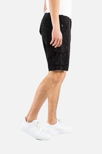 Bermudas negras de cargo hechas de tela, con bolsillos laterales y un corte relajado. Llevadas con zapatillas deportivas blancas.