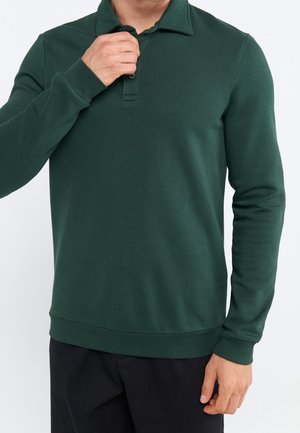 Polo à manches longues vert foncé avec un col à revers, une patte à deux boutons et des poignets côtelés. Tissu doux avec une texture lisse.