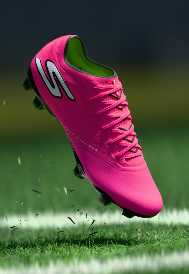 Taco de fútbol de color rosa brillante con suela y cordones negros levantando césped en un campo verde marcado.