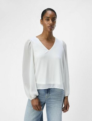 White, lightweight blouse with a V-neck and puffed long sleeves. Smooth texture, loose fit, paired with light blue jeans. Minimalist design.