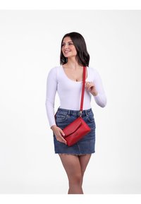 Červená kožená kabelka přes rameno s texturovaným povrchem, obdélníkovým tvarem a klopovým uzávěrem. Nastavitelný popruh pro všestranné nošení.