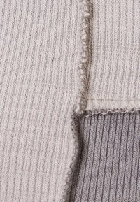 Tessuto a maglia di colore chiaro con texture a costine, cuciture visibili e finitura liscia ai bordi.