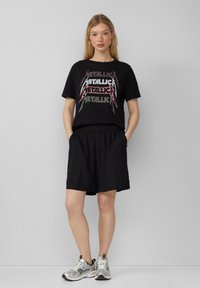 Zwarte t-shirt met metallic "Metallica" opdruk, gecombineerd met zwarte shorts met elastische tailleband en zilveren sneakers. Eenvoudig ontwerp, casual fit.