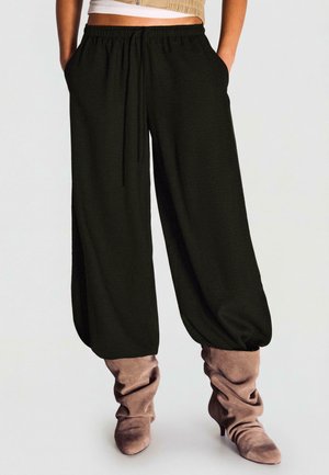 Čierne voľné nohavice s elastickým pásom a šnúrkou, v kombinácii s voľnými taupe semišovými čižmami so špicatou špičkou a vysokými podpätkami.