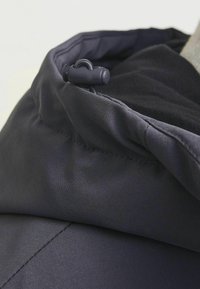 Mørkeblå jakke med blød tekstur, der fremhæver en nærbillede af hættens justerbare snore og elastiske kantdetaljer.