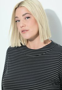 Schwarz-weiß gestreiftes Oberteil mit rundem Halsausschnitt und kurzen Ärmeln. Das Material wirkt weich und hat eine glatte Textur. Nahaufnahme-Porträt.