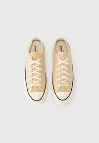 Κρεμ πάνινα αθλητικά παπούτσια με μπεζ λεπτομέρειες, λευκά κορδόνια και μαύρες καουτσούκ σόλες. Στρογγυλερή μύτη με αντιθετικό κάλυμμα και μινιμαλιστικό σχέδιο.