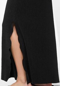 Juoda tekstūruota suknelė su šonu įpjovimu, kuriame yra banguotas kraštas. Audinys turi vertikalią ripsavimo raštą.