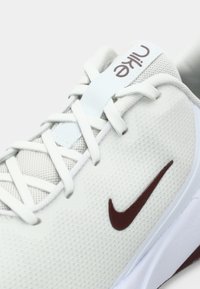 Λευκά αθλητικά παπούτσια με υφασμάτινη υφή στο πάνω μέρος, διακοσμημένα με καφέ σήμα Nike, λευκά κορδόνια και ανοιχτό μπλε λεπτομέρειες στη γλώσσα.