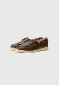 Brown leather boat shoes with a smooth surface, gold-tone eyelets, and a beige rubber sole featuring a slight heel and rounded toe.