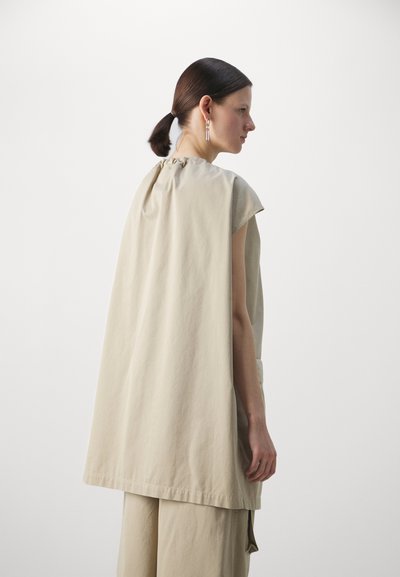 Top beige oversize senza maniche con scollo arricciato, realizzato in un tessuto morbido, caratterizzato da una vestibilità rilassata che si adagia sul corpo.