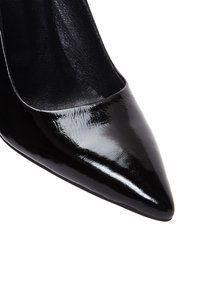 Chaussure à talon haut en cuir verni noir avec un bout pointu, une texture lisse et un design épuré, présentant une découpe sur les côtés.