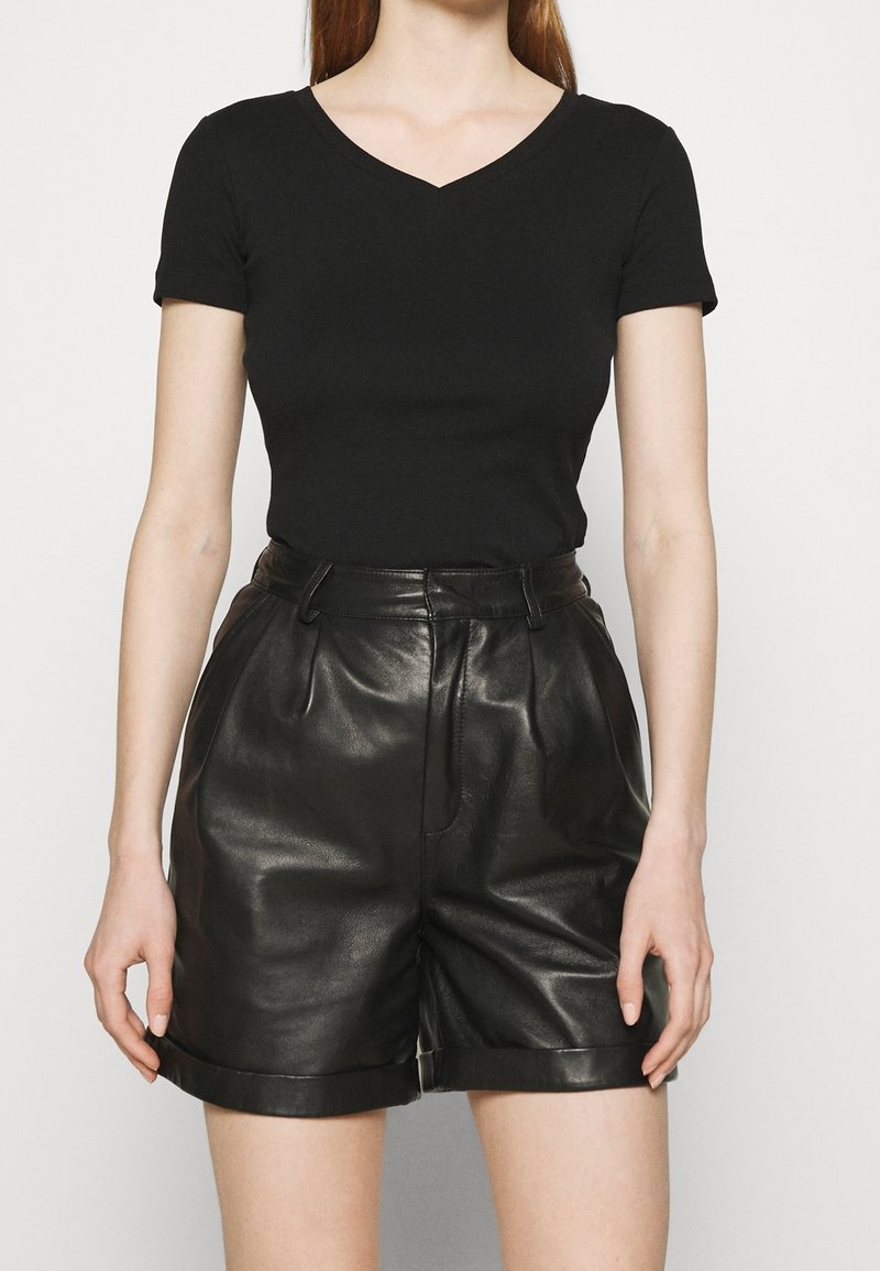 Sort kortærmet V-hals top parret med høj talje sort læder shorts med rullekanter og en glat, blank overflade.