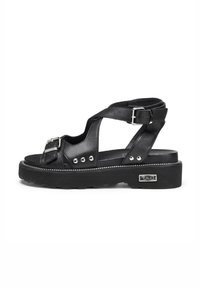 Sandali neri in pelle con larghe cinghie, dettagli con fibbia e borchie argentate. Sole spesso texturizzato con un bordo cucito bianco.