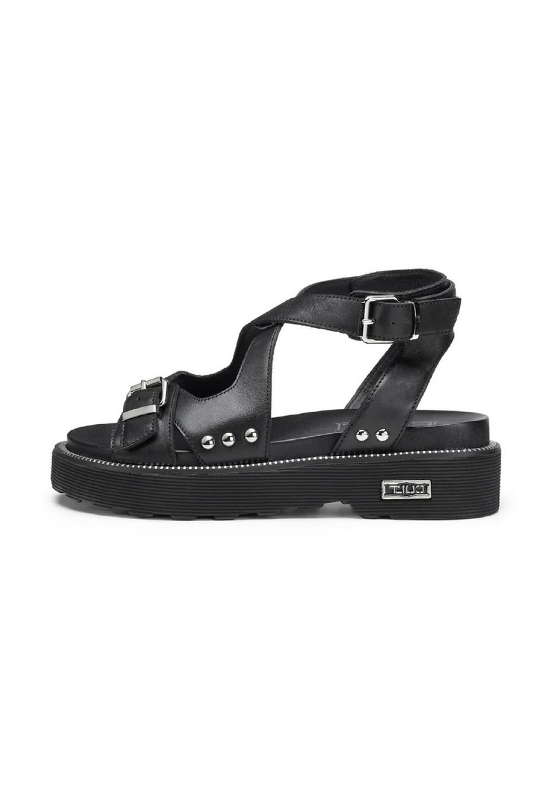 Sandali neri in pelle con larghe cinghie, dettagli con fibbia e borchie argentate. Sole spesso texturizzato con un bordo cucito bianco.
